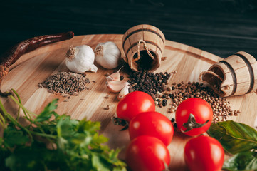 Spices: chili, black pepper, garlic, cumin, coriander, sweet pepper lie on a brown round wooden board on a black table. Place under the text.