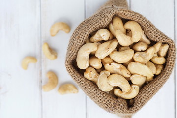 Pile of cashew nuts in sackcloth pouch on white wooden desk.