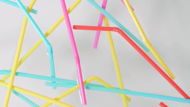 Close on brightly colored plastic single use bendable straws being dropped quickly into water against a neutral white background
