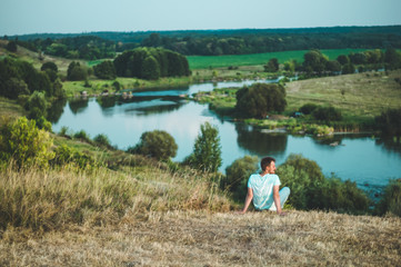 Naklejka na ściany i meble Young Man Sitting on a hill in a grass and enjoying the majestic landscape of nature and Enjoying the View. Winner Success concept