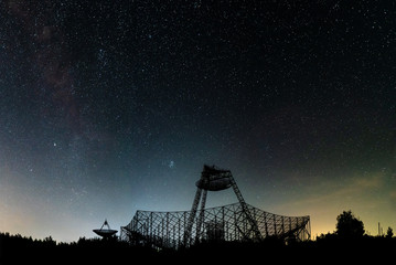 The group of antennas of the station of exploration of an ionosphere. A silhouette against the background of the night sky with glow and stars.