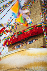 Buddha's eyes depicted on a buddhist stupa Boudnath, with many flutter flags of lunghta around.