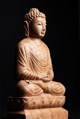 Buddha in a meditation pose of a whole lotus. Statue made of wood, isolated on a black background.