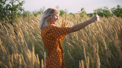 attractive fun hippie blonde woman in the field at sunset making a selfie with a bouquet