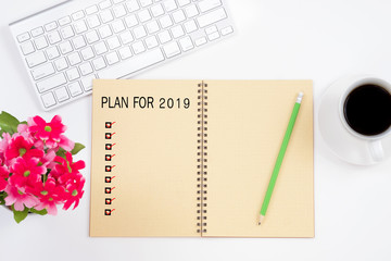 Note book with plan for 2019 word and check marks, keyboard, red flower, pencil and a cup of coffee on white table background.