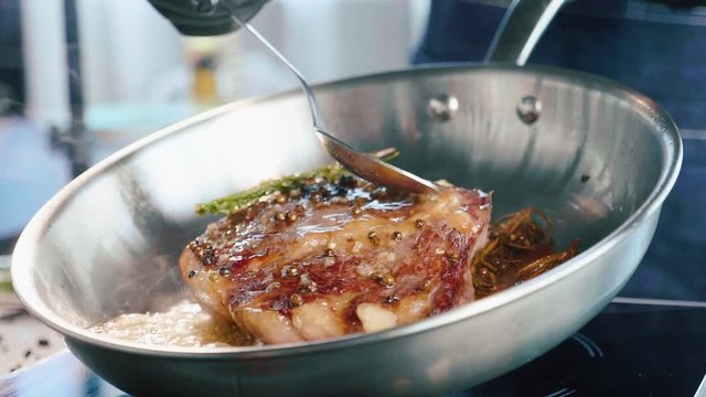 Meat steak is fried in butter and grease on frying pan, close-up in slow motion.