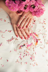 Obraz na płótnie Canvas Beautiful woman hands with perfect violet nail polish on white wooden background holding little quartz crystals, decorated with rose leaves, healing crystal concept shoot, can be used as background 