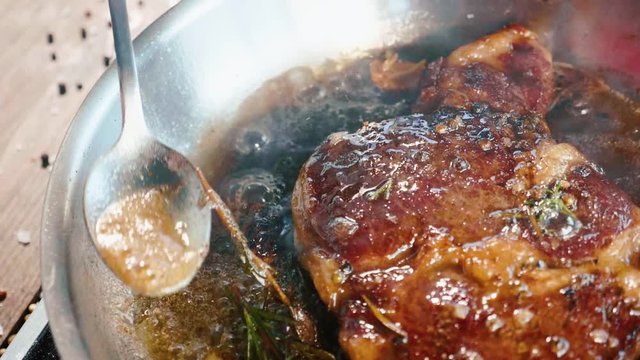 Meat steak is fried in butter and grease on frying pan, close-up in slow motion.