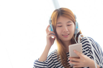 Naklejka premium Beautiful asian young woman enjoy listen music with headphone and holding smart mobile phone while sitting in bedroom, relax girl with earphone, leisure and technology concept.