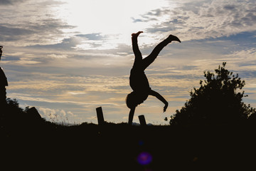 silhouette happy child playing upside down outdoors in summer park walking on hands at sunset