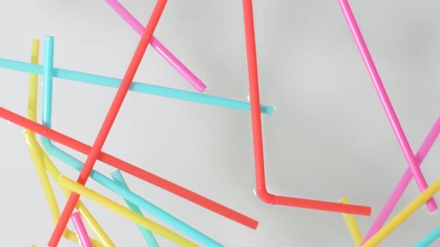 brightly colored plastic single use straws dropping into water against a neutral white background,