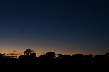 sunset with waning moon and silhouettes of houses