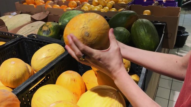 Hands of a caucasian young woman chooses melon in a glocery shop.