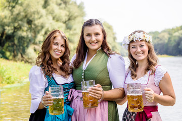 Oktoberfest Freunde in Lederhosen und Dirndl trinken Bier an der Isar