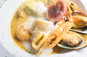 top view of fusion food ingredients with crap, New Zealand mussels, shrimp and red squid pored with white sauce on orange soup.