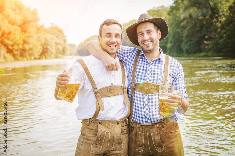 Wall mural Oktoberfest Freunde in Lederhosen und Dirndl trinken Bier an der Isar