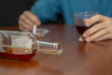 primer plano de una botella y fondo hombre bebiendo y fumando