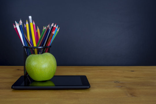 Tableta digital y manzana en el escritorio frente a la pizarra
