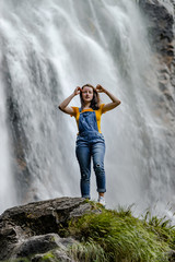 Young teenage girl standing on the big stone near waterfall