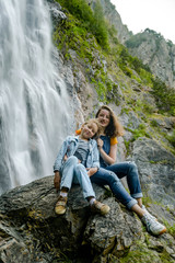 Two sisters sitting on the stone on waterfall background