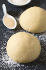 Risen or proved yeast dough balls for bread or pizza on a floured slate surface, ingredients in the back, photographed with natural light (Selective Focus, Focus on the front of the dough ball)
