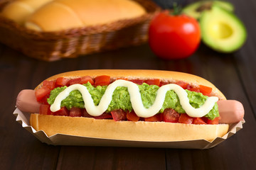Chilenischer Completo Italiano Hotdog gefüllt mit Würstchen, Tomate, Avokado, und Mayonnaise, fotografiert mit natürlichem Licht (Selektiver Fokus, Fokus auf die Vorderseite des Hotdogs)