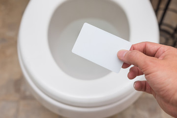 Holding blank card (credit card, membership card, coupon, drivers license) into toilet; bright and clean; finance concept