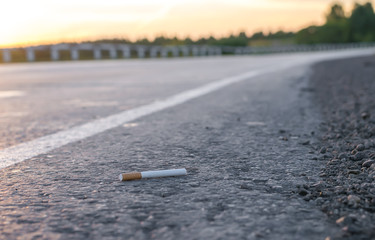 View of cigarette lying on the asphalt on a country road in the evening