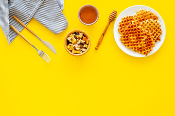 Hot round waffles ready to eat. Belgian recipe. Waffles on plate near honey and dried fruits on yellow background top view copy space