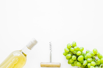 Open the wine concept. White wine in glass bottle near bunch of grapes and corkscrew on white background top view copy space