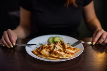 Woman eating delicious quesadilla in restaurant. Close-up of the hands of a girl eating Mexican food