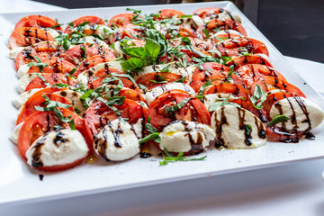 Caprese salad with mozzarella tomato, basil and balsamic vinegar arranged on white plate