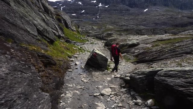 Male tourist is coming down the hill in Norway at Trolltunga path with backpack at the summer.