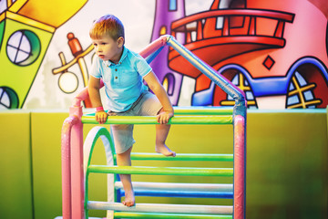 Cute little boy in a blue T-shirt is playing on a children's playground indoors.