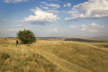 Summer landscape of fields and meadows with harvested crop, boundless expanses, blue sky with cumulus clouds, top view from mountain. Girl takes pictures of beautiful nature.