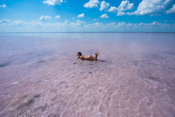 A beautiful woman in a bikini is lying on her stomach in a pink salt lake. The red-haired woman lies, sexually bending in her back and lifting her ass.