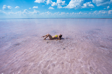 Fototapeta na wymiar A girl in a yellow bikini is lying on her back in a pink salt lake. the bottom of the lake is covered with salt. the lake is pink because of the red algae. The girl lies on her back, leaning on her el