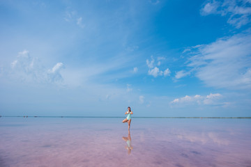 Fototapeta na wymiar A beautiful woman in a mint body stands in a tree position in a pink salt lake. Redhead young woman doing yoga standing ankle-deep in water, pink salt lakes Bursol'