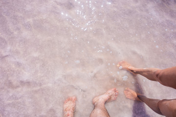 A man and a woman stand barefoot in a pink lake. Feet in the salt lake. The couple is barefoot in the salt pink lake Bursol, Altai territory