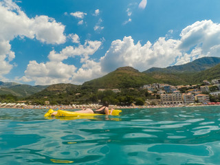 woman on yellow mattress in water suntanning landscape of beach side in montenegro