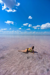 Obraz premium A beautiful red-haired girl in a yellow bikini lies on her side in a pink lake in Altai. Rose lake is a salt Deposit.