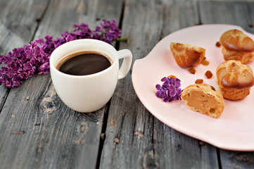 Cup of coffee, cakes and branch of a lilac on a gray wooden background