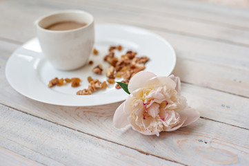 Cup of coffee with milk, nuts, sweets and a bud of a peony on a white saucer