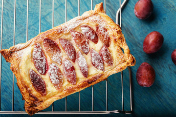 Homemade puff pastry flan with plums on dark blue background. Delicious rectangular galette top view