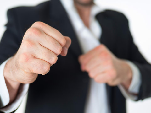 Confident businessman, stands with his fists in a boxing rack against a white wall. Fists close-up