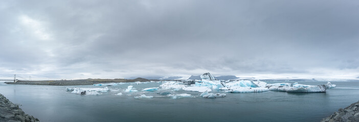 A large panoramic image of Jokulsarlon Glacial Lagoon with numerous icebergs visible floating in the lagoon.