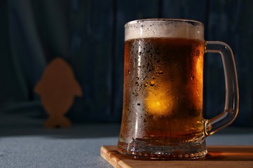 Still life of mug of cold light draft beer on a table with fish on a blue background