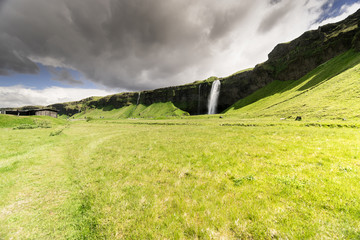 Unrecognizable tourists occupy the path leading towrads the waterfall Seljalandsfoss, one of the stops on Iceland's popular tourist route the golden circle.