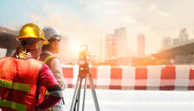 Surveyor builder and engineer working with theodolite transit equipment at construction site outdoors on street in sunlight in the city background