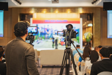 Video camera operator working with his equipment at indoor event. 